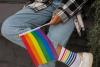 The lower half of a person in denim jeans and a checked shirt, with the central focus on them holding a rainbow LGBTQ+ Pride flag